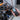 A hand holding a black and orange handheld diagnostic tool with a flexible probe, positioned in front of a large industrial machine with copper and black pipes.